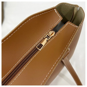 Détail de la fermeture éclair dorée et coutures blanches sur un sac cabas marron
