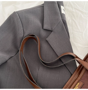 Détail d'un grand sac cabas marron en cuir avec étiquette sur une veste de blazer grise