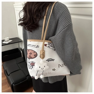 Detail of white canvas tote with astronaut print, leather trim, and plush cloud charm