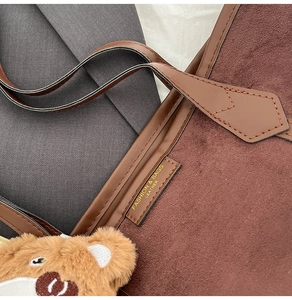 Détail du cabas en daim marron foncé avec garniture en cuir et breloque ours peluche