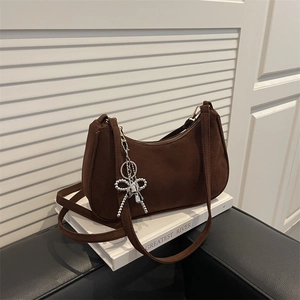 Brown frosted suede underarm bag with a silver bead bow charm on a white book