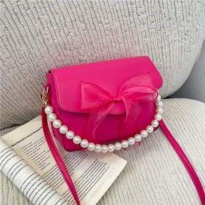 Fuchsia crossbody bag with satin bow, pearl chain and leather strap on sofa background