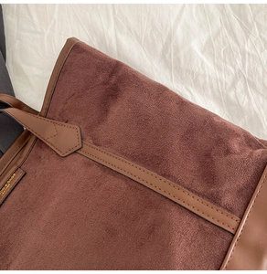 Gros plan d'un cabas en daim marron avec anses en cuir et logo doré estampillé sur le côté