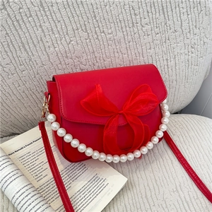 Elegant red crossbody bag with mesh bow, pearl handle, and red leather strap on book