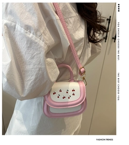 Mini cherry print crossbody bag with pink strap shown from a side view on a model