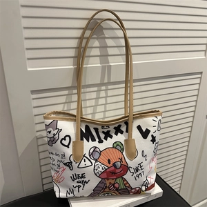 White graffiti canvas tote bag with brown leather straps shown on a white book