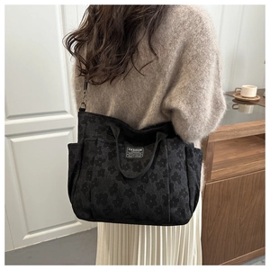 Detail of black tote bag with embossed daisy patterns and Fashion label on sweater