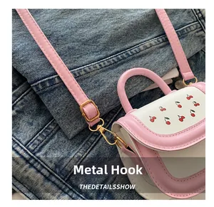 Close-up of golden hardware hooks and adjustable pink strap on a cherry pattern bag