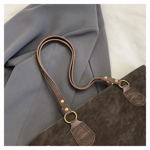 Nahaufnahme einer braunen Wildleder-Tragetasche mit goldenen Metallringen und Ziernähten