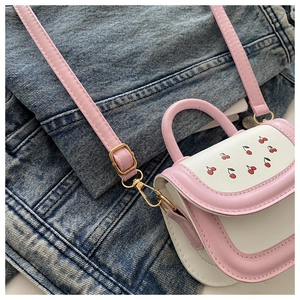 Detailed view of pink and white mini cherry handbag with golden hardware on denim