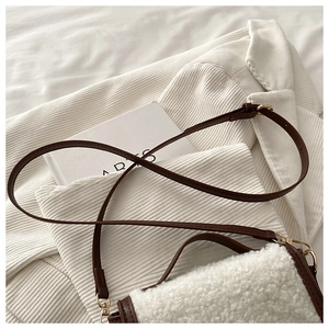 Detail of white faux fur saddle bag with brown leather trim and golden metal buckles