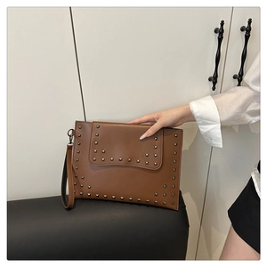 Detailed view of a brown leather envelope clutch featuring silver square rivets and wrist strap