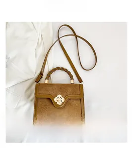 Close-up of brown suede crossbody bag featuring a golden flower clasp and woven handle