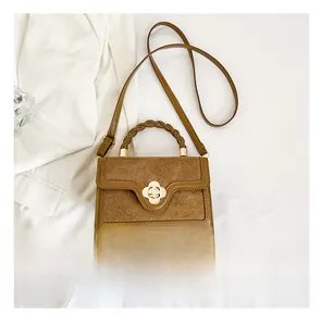 Brown leather handbag with woven handle and gold floral clasp, shown next to a smartphone