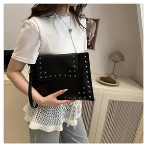 Detail of a black leather envelope clutch with silver rivets held by a model in a minimal room