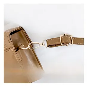 Close-up of light gold metal hook and adjustable shoulder strap on brown leather handbag