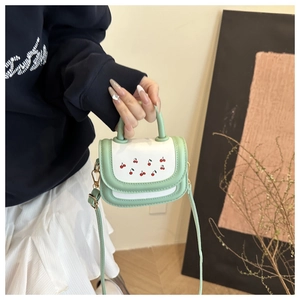 Detail of mint green and white crossbody bag with cherry print held by hand