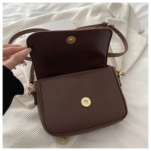 Detail of dark brown saddle bag showing gold magnetic closure and textured leather