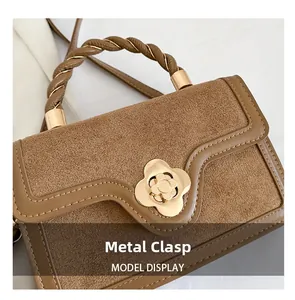 Detail of a brown suede handbag with a golden flower buckle and woven handle