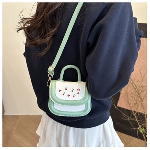 Detail of mint green cherry print mini square bag worn as a crossbody shoulder bag