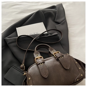 Detail showing vintage brown bowling bag with bronze buckles and refined stitching texture