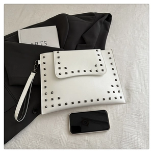 Detail of white envelope clutch bag with black square studs and removable wrist strap