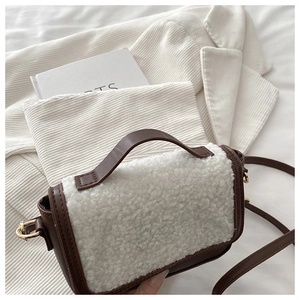 Detailed close-up of a white faux shearling saddle bag with brown leather trim and gold buckle