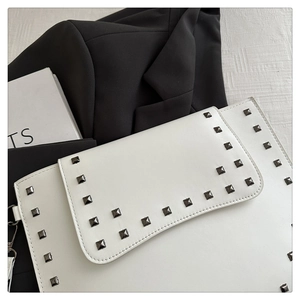 Detail of white leather envelope clutch featuring metallic square rivets and flap design