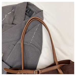 Detail of a brown suede tote bag featuring slim leather straps and silver metal buckles