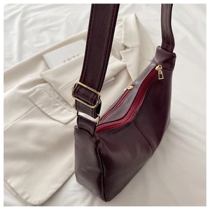 Detail view of burgundy PU leather shoulder bag with golden zippers on white blazer