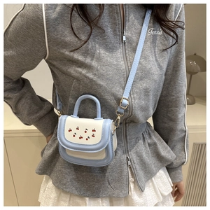 Close-up of a mini cherry print handbag with light blue and cream stitching and metal strap