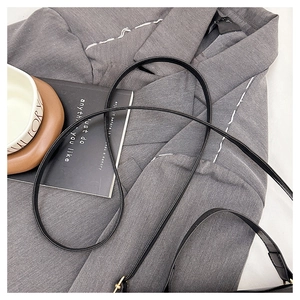 Detail of slim black faux leather shoulder strap with metal hardware on grey blazer
