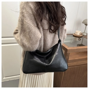 Close-up detail of glossy black faux leather underarm bag featuring a minimalist central seam