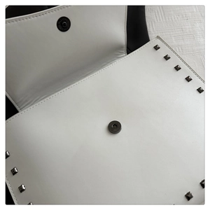 Detail view of white leather envelope bag showing metal studs and magnetic snap closure