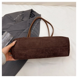 Detail view of the wide bottom structure and stitching of a dark brown suede tote bag