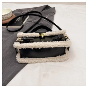 Detail of black leather handbag with white faux fur trim and gold buckle closure