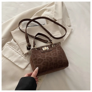 Detailed view of leopard print square bag with gold metal twist lock on beige fabric