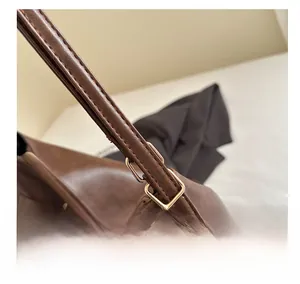 Close-up of golden adjustable buckle on brown leather shoulder bag with neat stitching