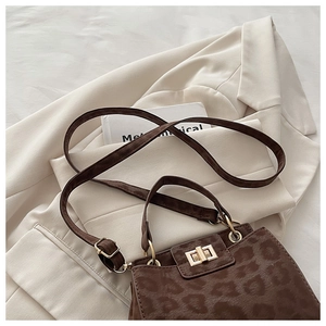 Detail of leopard print suede handbag with gold lock and shoulder strap on white blazer