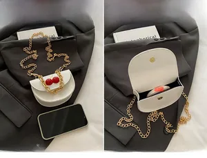 Detail view of white mini crossbody bag featuring cherry ornament and gold chain strap