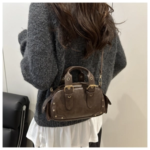Close-up of vintage brown motorcycle bag with studs and belt details on gray sweater