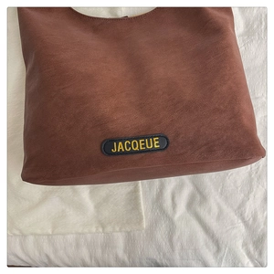Detail of dark brown leather tote bag showing a stitched label on a white linen surface