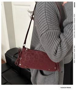 Detail of burgundy leopard print crescent bag featuring side bows and silver rivets