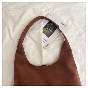 Flat lay of vintage brown leather hobo shoulder bag on soft white linen fabric background