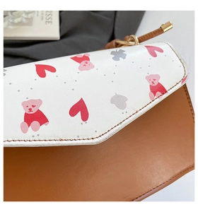 Detailed close-up of brown leather bag featuring white heart and bear print flap
