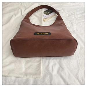 Detail of the brown leather tote bag showing wide shoulder strap and textured logo patch
