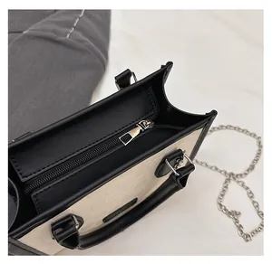 Close-up of smooth silver zipper and black leather trim on a beige checkered tote bag