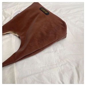 Detail shot of the dark brown leather hobo tote bag featuring a gold JACQEUE brand label