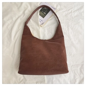 Flat lay of dark brown matte leather hobo bag with wide strap on white fabric background