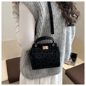 Detail of black leopard texture handbag with golden square lock on elegant gray outfit